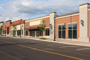 Empty brick shopping center with storefronts and a cloudy sky.